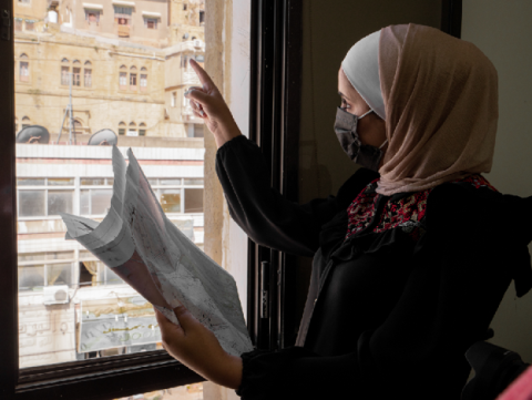 This photo depicts Asma Arabiyat, a young engineer pointing at old buildings in Al-Salt City, Jordan on May 18, 2021, while holding a street naming and building numbering map. USAID is supporting nine municipalities in Jordan to install street signs and building numbers to facilitate service delivery and foster economic development. Photo Credit: Omar Khiyami, Trademark contracted by USAID CITIES